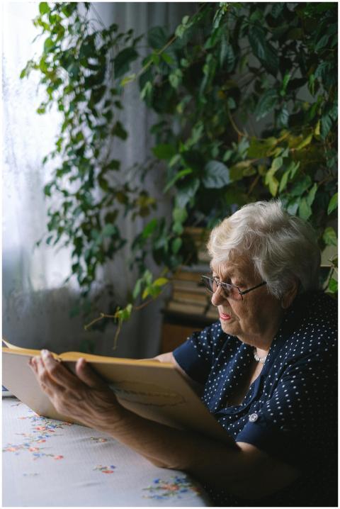 Senior woman with glasses reading a large book at