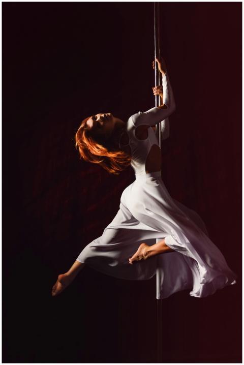Graceful pole dancer in white dress showcasing str