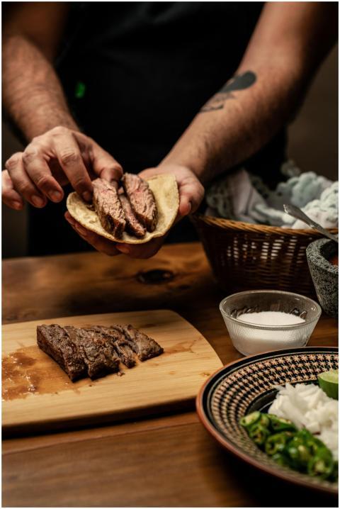 Close-up of hands preparing a steak taco with fres