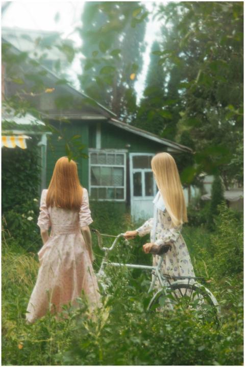 Two women in vintage dresses stand beside a bicycl