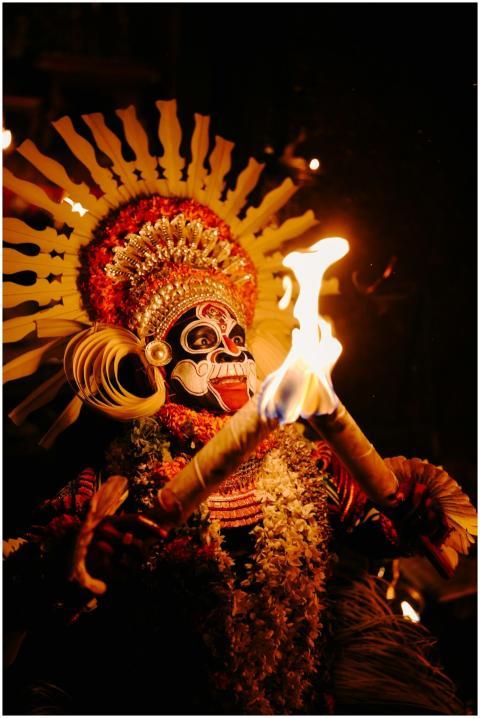 A vibrant Theyyam performer holding fire torches d