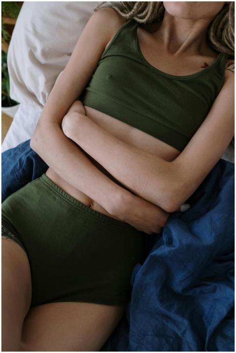 A woman in green clothing lies on a bed clutching