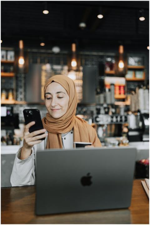 A woman in a hijab is smiling while using a smartp