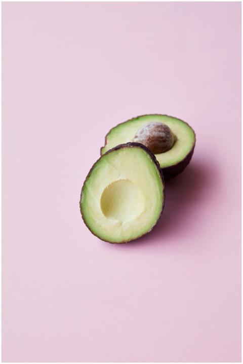 A fresh halved avocado displayed on a pastel pink