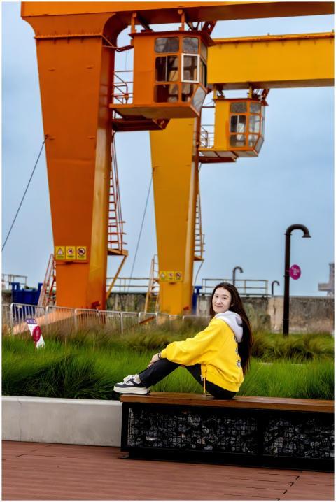 A young woman in a yellow hoodie sits on a bench n