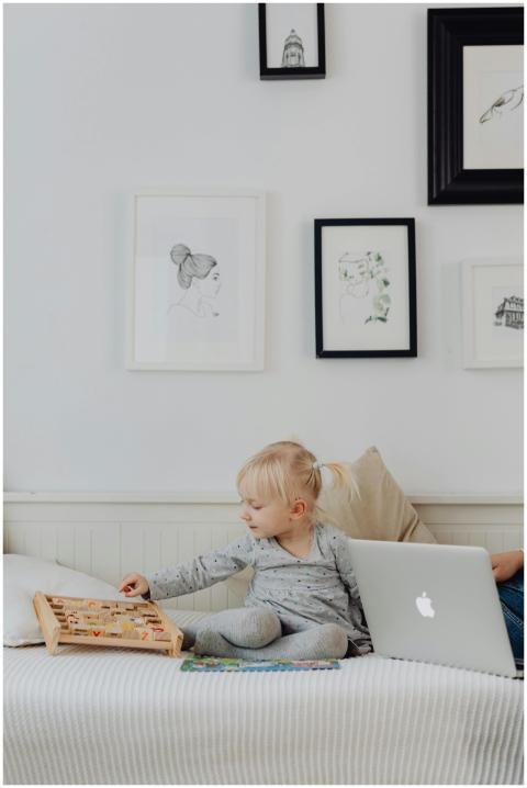 A cute child in a gray sweater sits on a bed playi