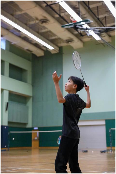 A young boy playing badminton in an indoor gym, fo
