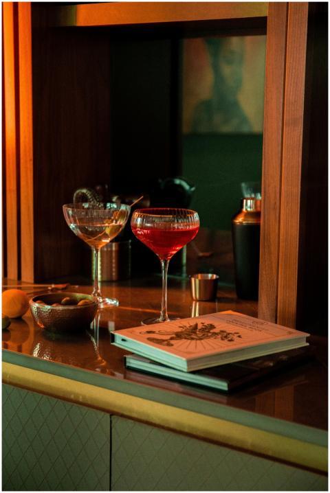 A stylish bar scene with red cocktail, glasses, bo