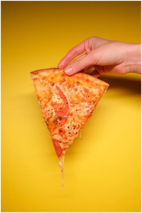 Hand holding a cheesy pizza slice against a vibran