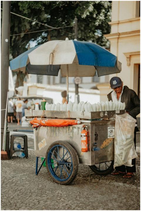 A street vendor with a blue umbrella cart selling