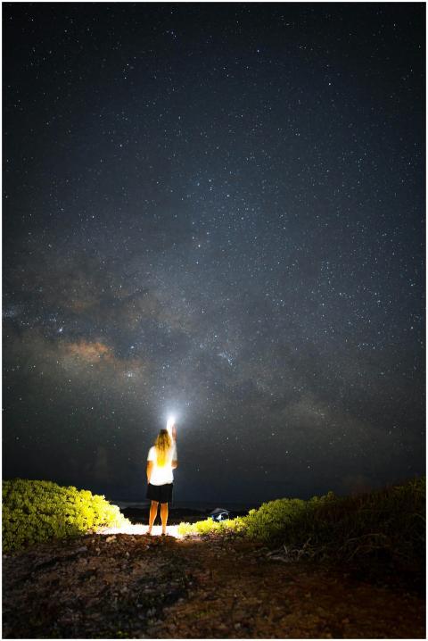 A person stands under the night sky, illuminated b