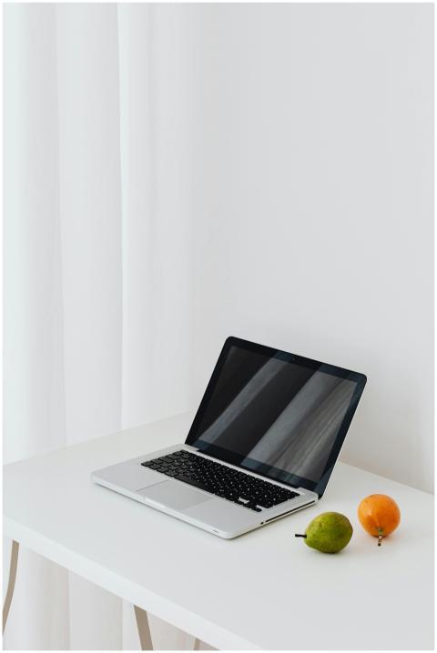 A sleek laptop on a white desk with fruits, showca