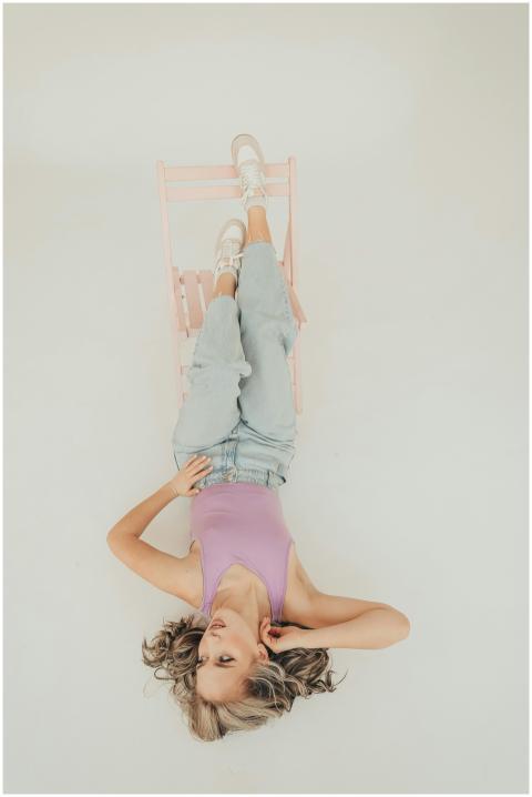 A stylish woman lies upside down on a pink chair a