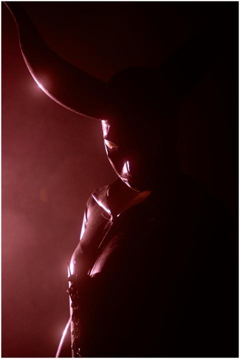 A shadowy figure wearing a horned mask, illuminate