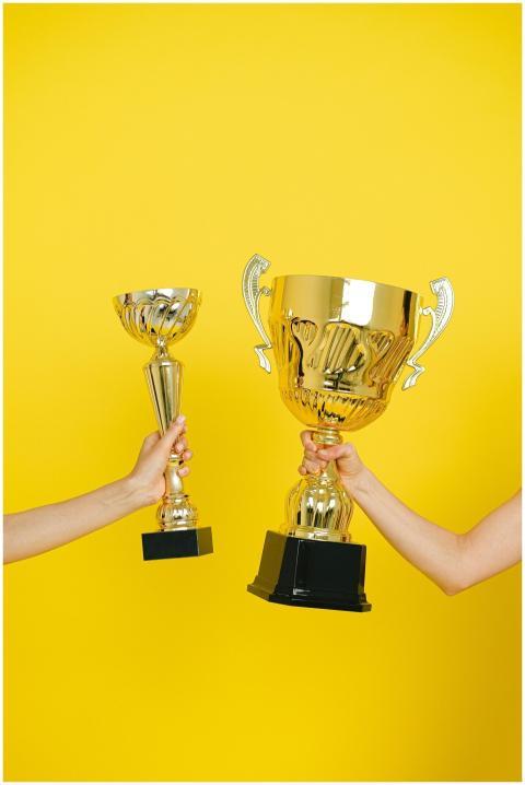 Two hands holding trophies against a vivid yellow