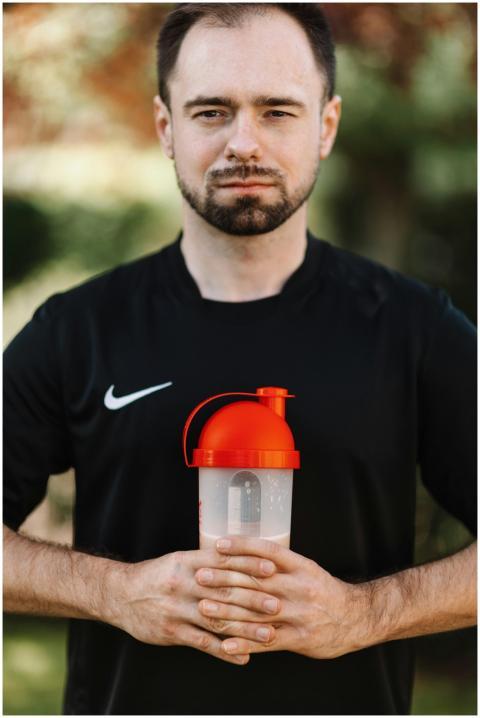 Bearded man in black shirt holding a protein shake