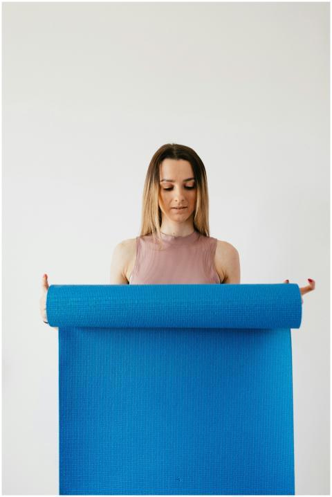 Young woman unfolding a blue yoga mat indoors, foc