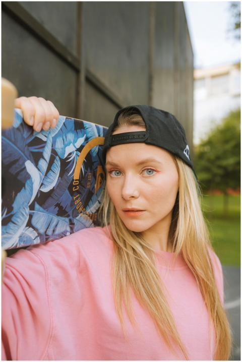 Blonde woman with skateboard in park wearing pink