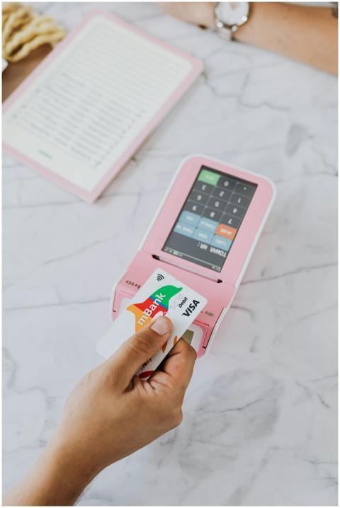 Close-up of hand swiping Visa card on pink POS mac