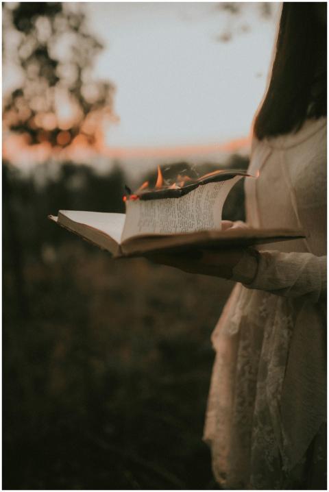 A woman holding a burning book in a park during fa