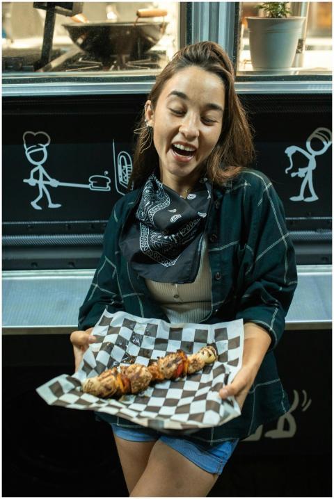 A joyful woman holding grilled skewers from a food