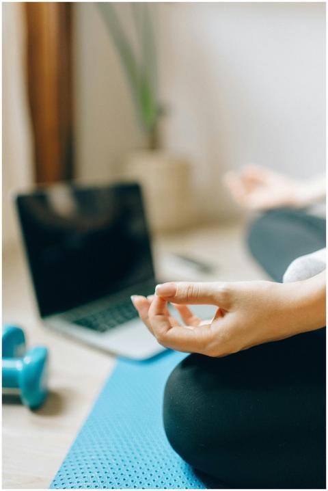 Adult woman meditating on yoga mat next to laptop