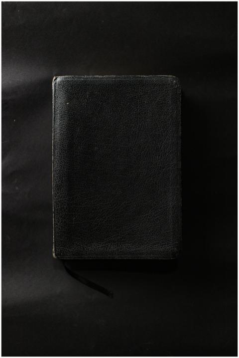 A closed black leather-bound book on a plain black