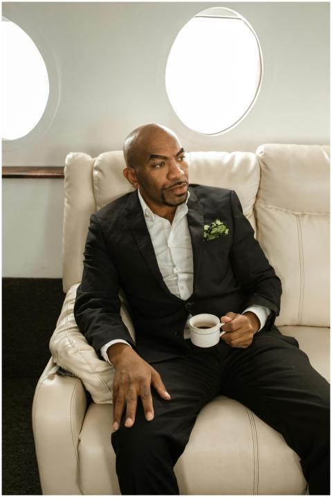 A bald black man in formal attire relaxes with a c