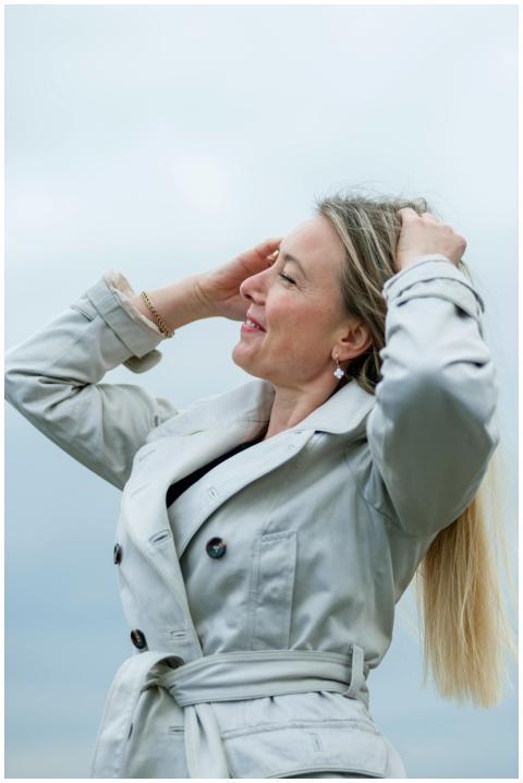 A woman in a light gray trench coat smiling and en