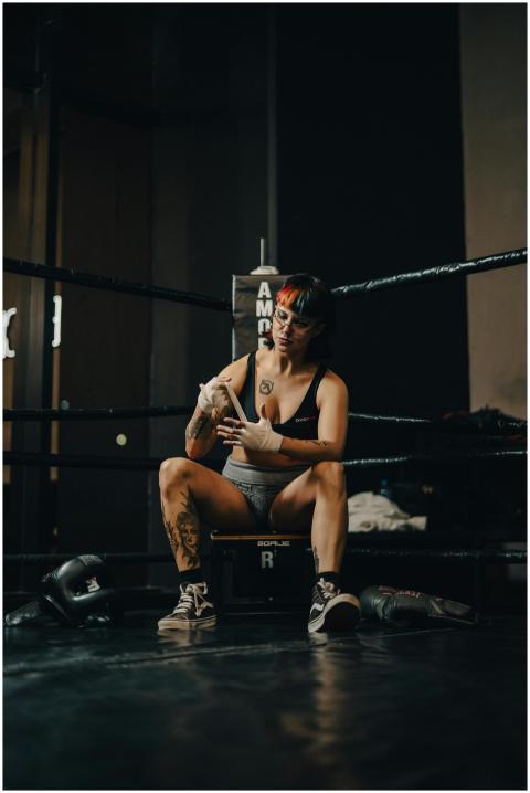 A female boxer wraps her hands while sitting in a