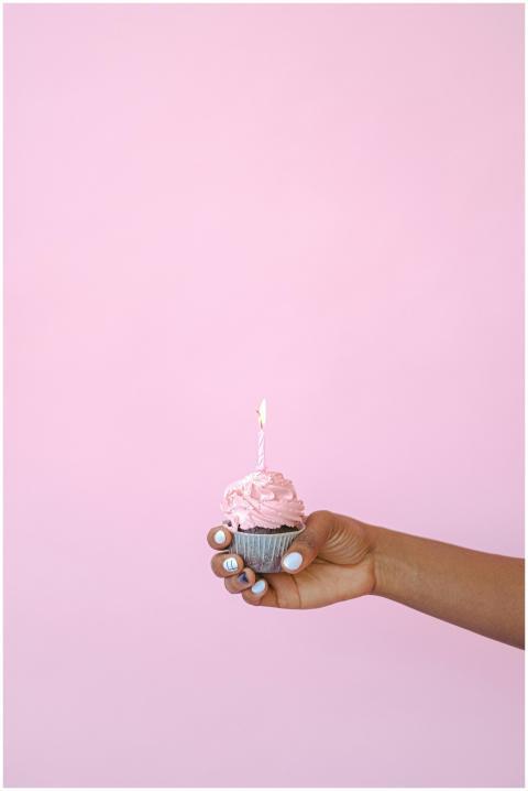 A cupcake with a lit candle held in a hand against