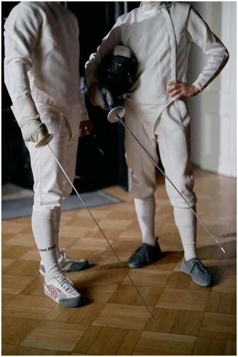 Two athletes in fencing attire with swords poised