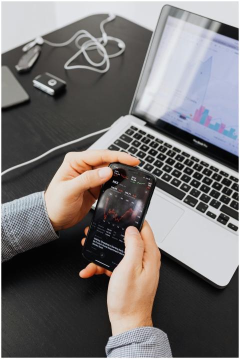Hands holding smartphone displaying stock charts b