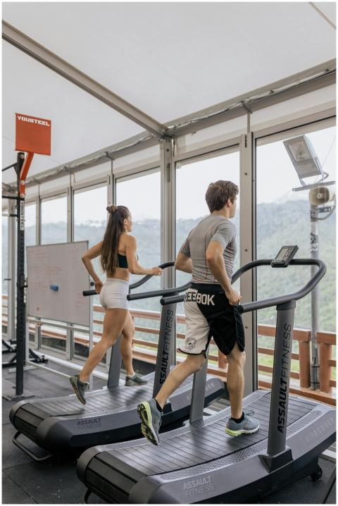 Man and woman running on treadmills in a bright gy
