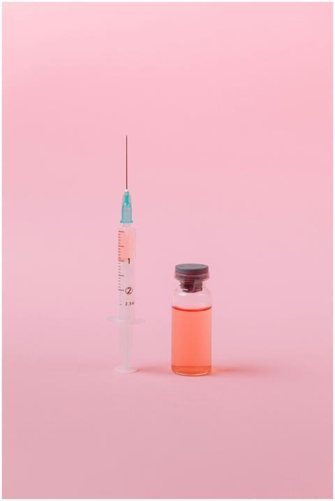 A syringe and vaccine vial on a pink background in