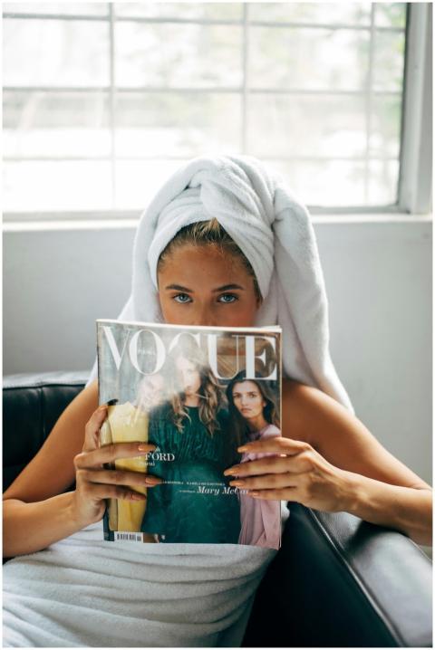 Woman wrapped in towel reading Vogue magazine in a