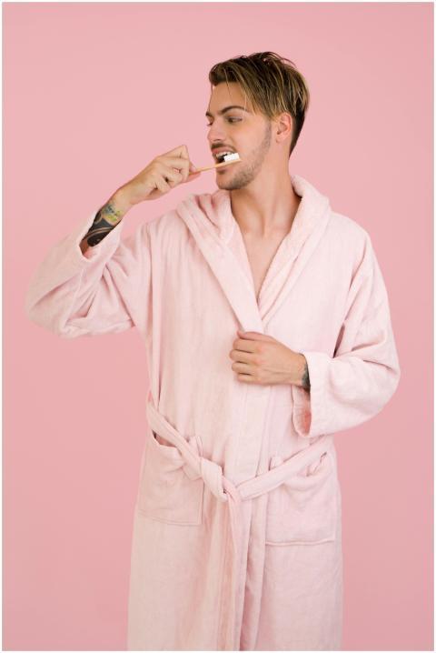 Young man in a pink bathrobe brushing teeth in fro