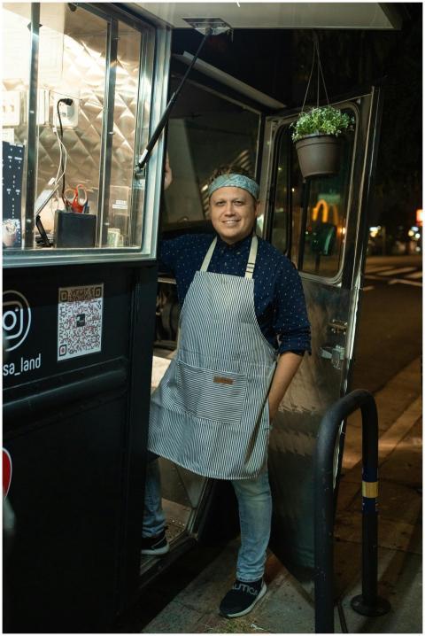 A friendly chef stands by a food truck on a bustli