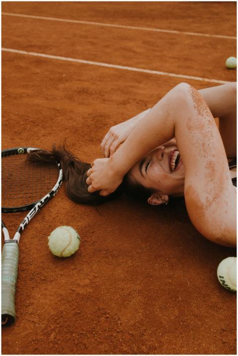A young woman laughing and lying on a clay tennis
