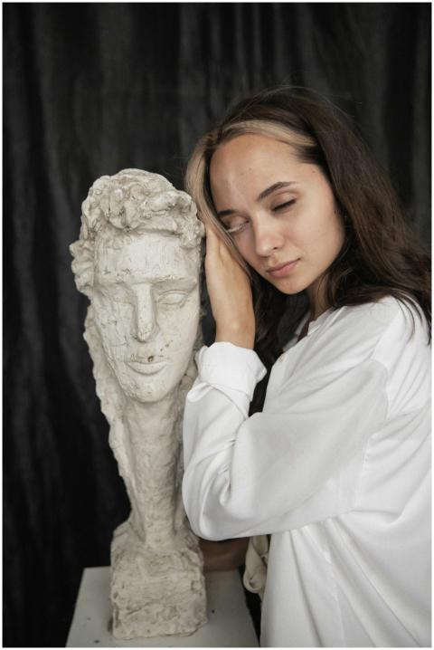 Woman in white shirt poses next to a gypsum sculpt