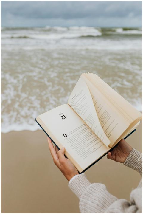 A person reads a book by the beach with waves in t
