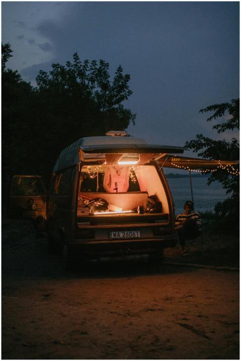 A person enjoys a peaceful evening by a lit camper