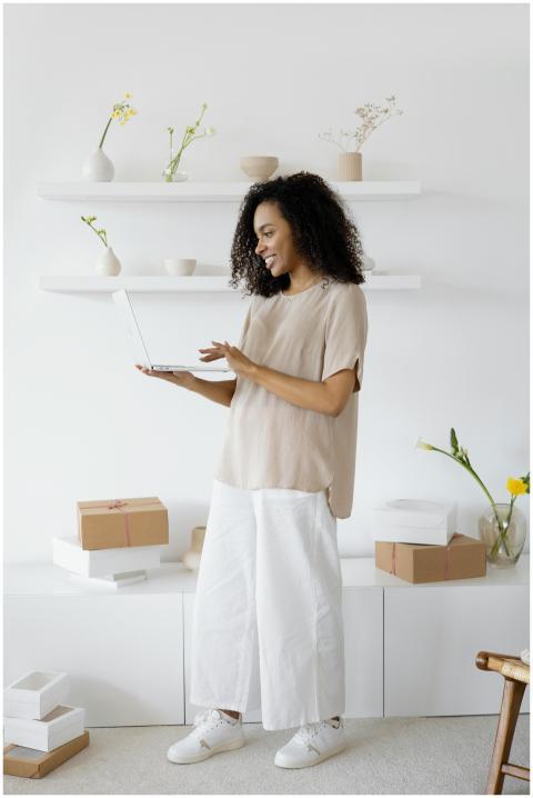 A smiling woman using a laptop surrounded by boxes