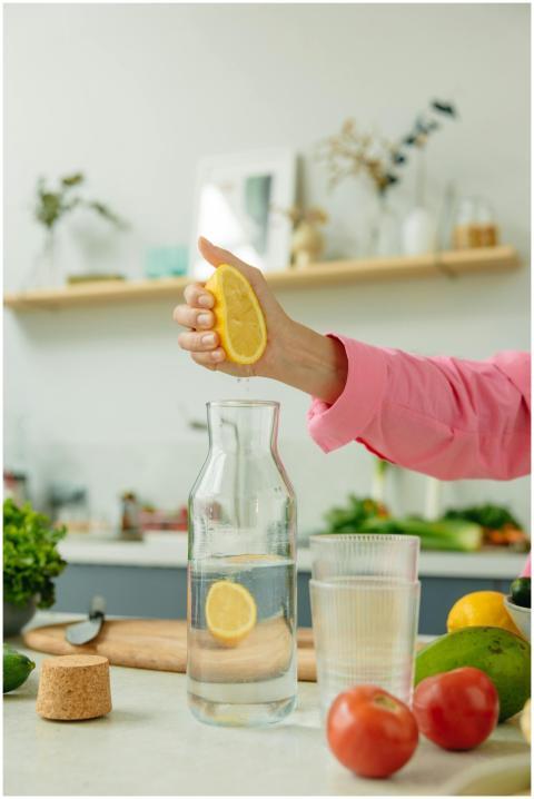 A person holds a lemon over a glass pitcher in a m