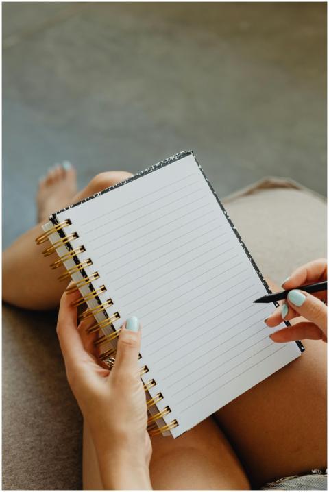 A person with manicured nails writes in a spiral n