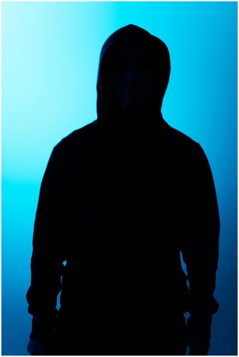 Silhouette of a hooded figure backlit by eerie blu