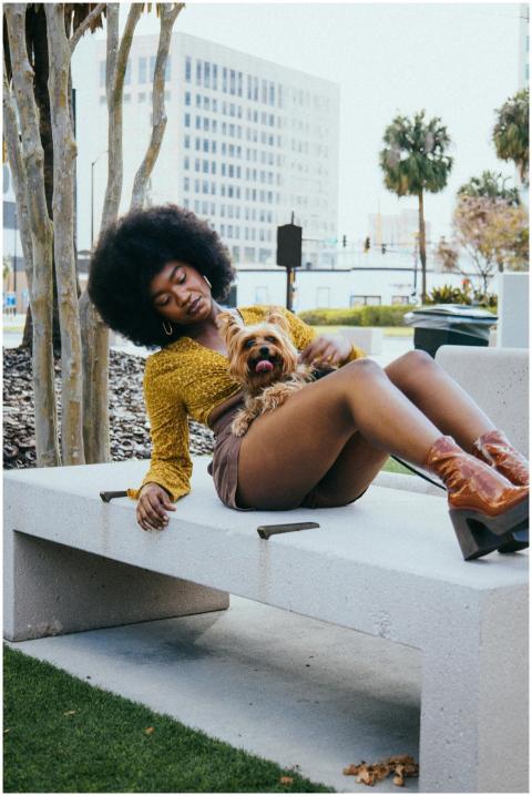 Fashionable woman with afro and dog sitting on a b