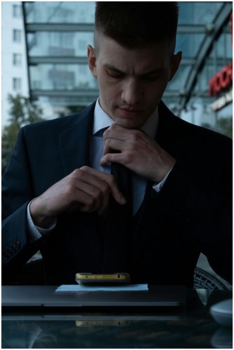 A young Caucasian man in a suit adjusting his tie
