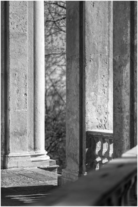 A sunlit stone balcony with ornate pillars casting