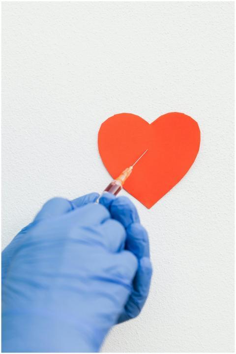 A gloved hand holds a syringe near a heart shape,